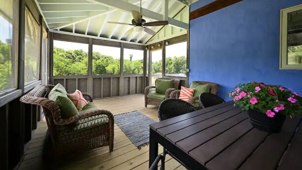 Une véranda couverte, avec des meubles en osier, une table et une plante en pot.