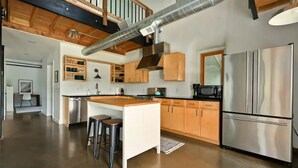Une cuisine spacieuse dotée d’un îlot central, de meubles en bois, d’appareils électroménagers en acier inoxydable et d’un système de conduits apparent.