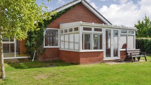 A conservatory attached to a brick house with a glass roof, a bench, and a grassy lawn. - 2 bedroom accommodation in Thorpe St Peter (Thorpe St Peter)
