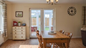 A dining area with a wooden table and chairs, a chandelier, a clock, and a sliding glass door leading to a patio. - 2 bedroom accommodation in Thorpe St Peter (Thorpe St Peter)