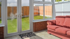 A conservatory with a glass door leading to a garden, a red sofa, and a tiled floor. - 2 bedroom accommodation in Thorpe St Peter (Thorpe St Peter)