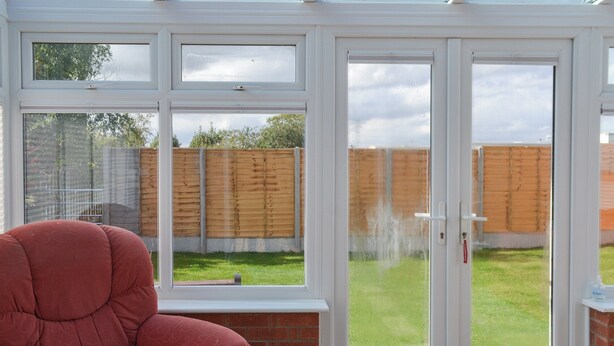 A conservatory with a red chair, a glass door, and a view of a grassy yard. - 2 bedroom accommodation in Thorpe St Peter (Thorpe St Peter)