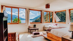 A bedroom with a large window offering a mountain view, a wooden bed, a bedside table, and a chair. - Stunning Luxury Eco Villa (Tzununa)
