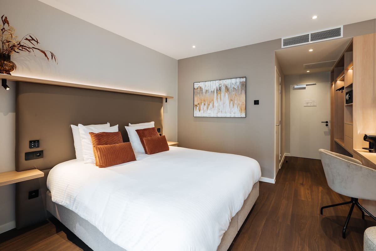 A modern hotel room with a large bed, bedside tables, a desk, and a chair.