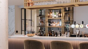 Zona de bar con mostrador, taburetes y una estantería con botellas y vasos.