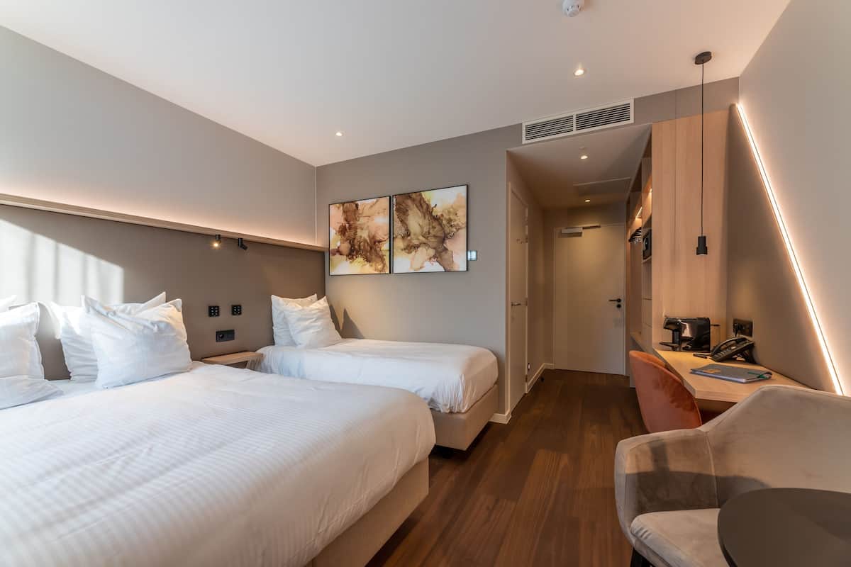 A hotel room with two beds, a desk, a chair, and artwork on the wall.
