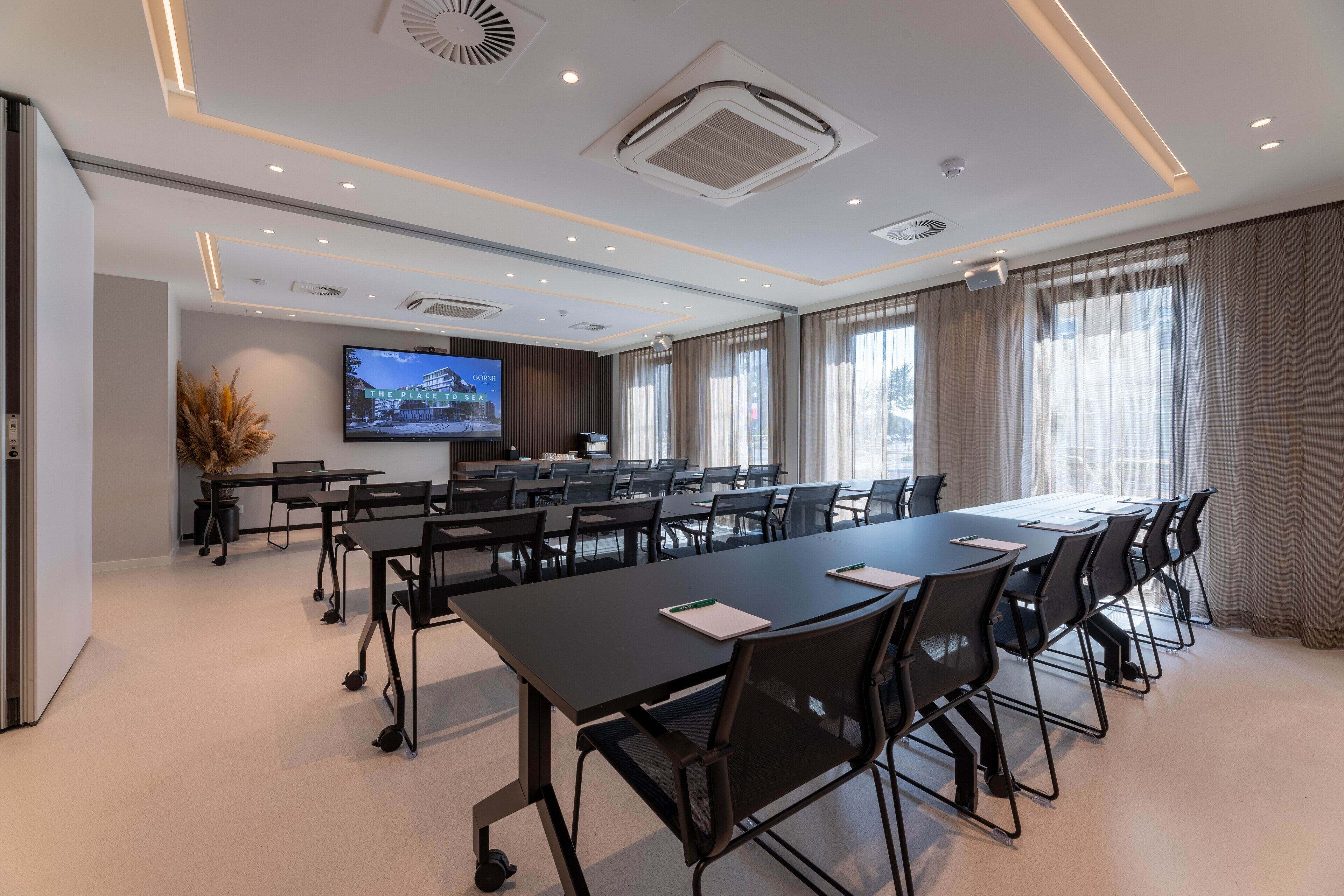 Una sala de conferencias moderna con una larga mesa, múltiples sillas y una pantalla grande.
