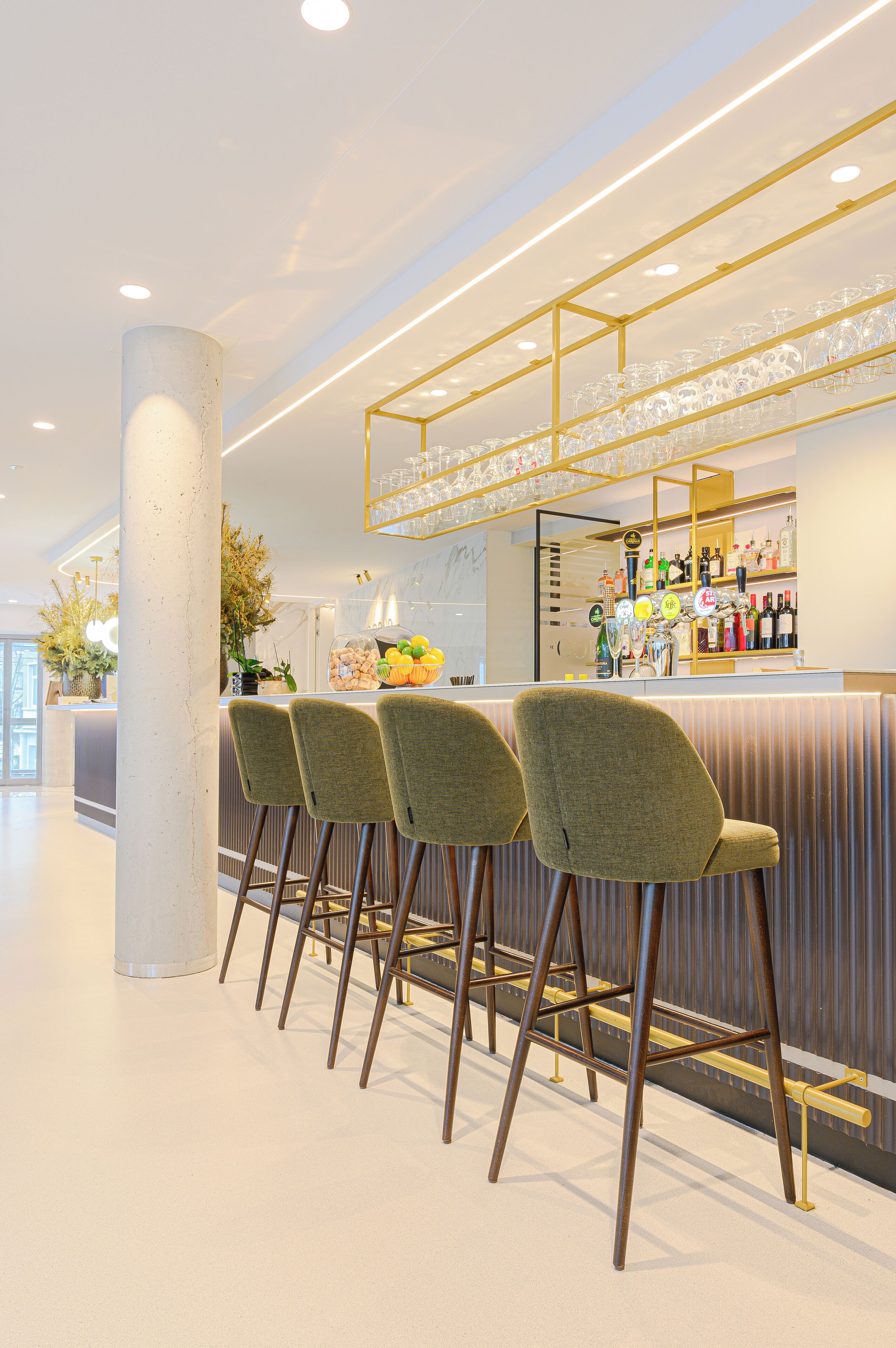 A modern bar area with a bar counter, stools, and a variety of bottles and glasses.