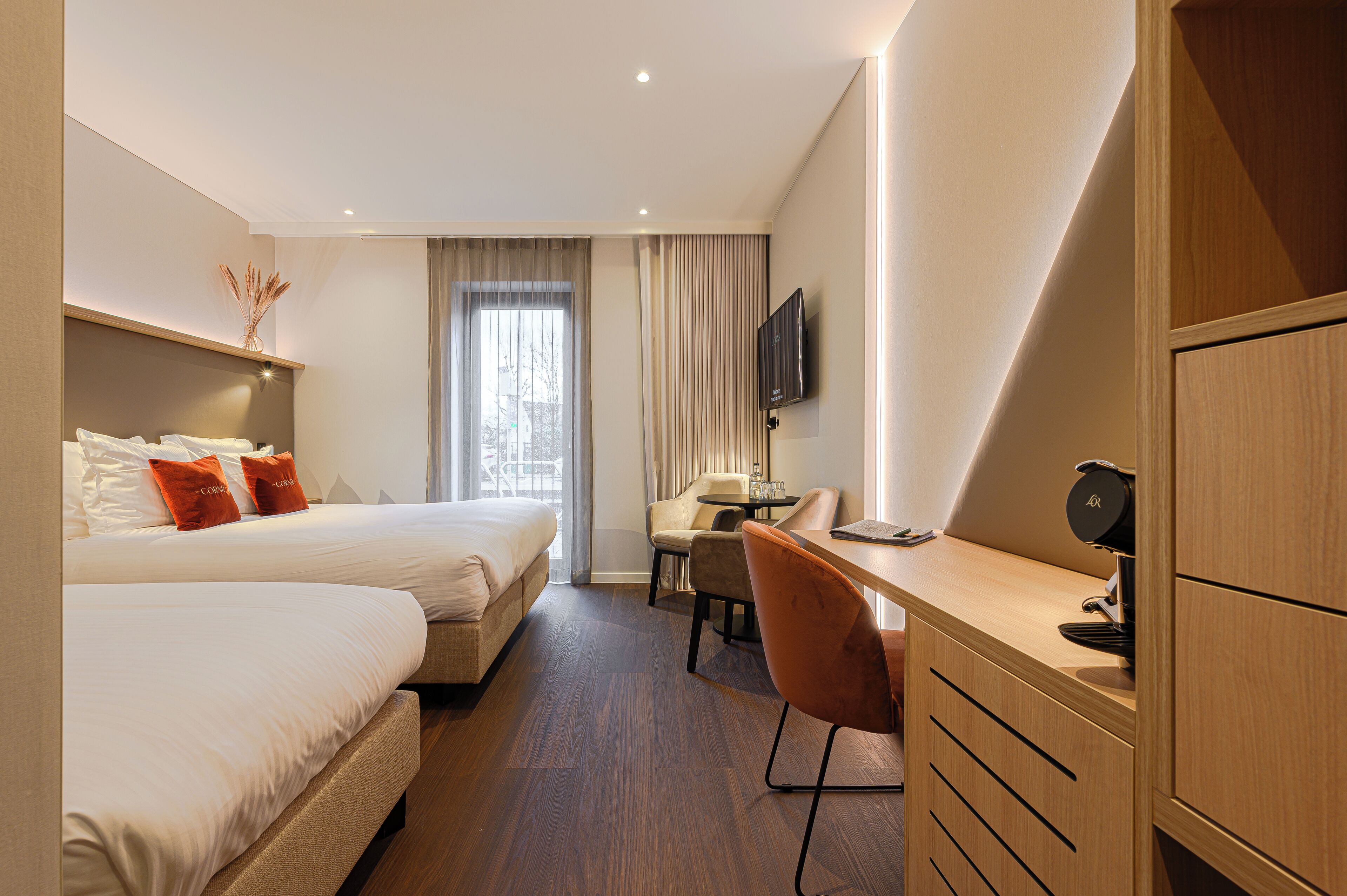 A hotel room with two beds, a desk, a chair, a TV, and a wardrobe.