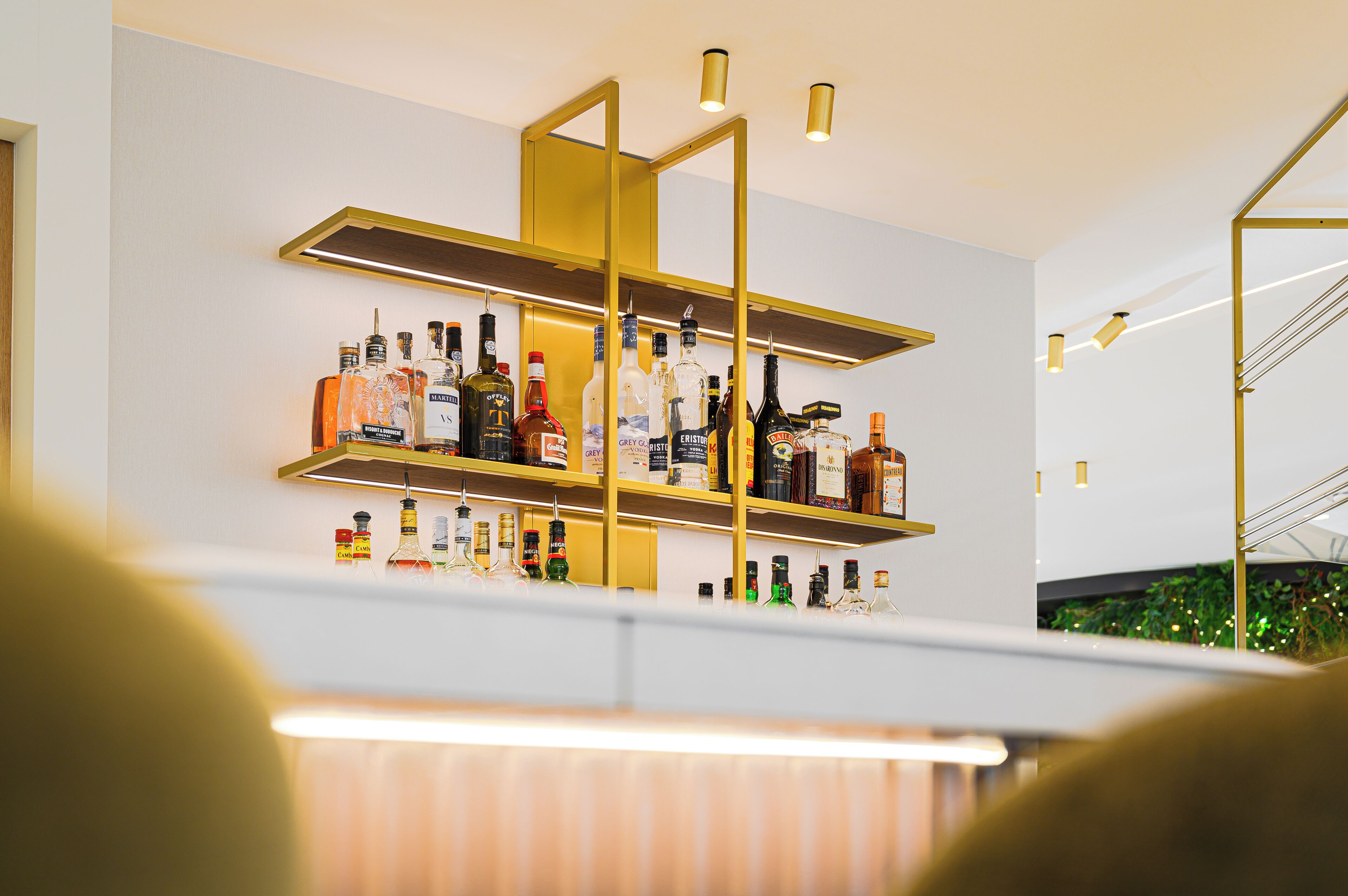A bar area with shelves of liquor bottles, a modern light fixture, and a plant in the background.
