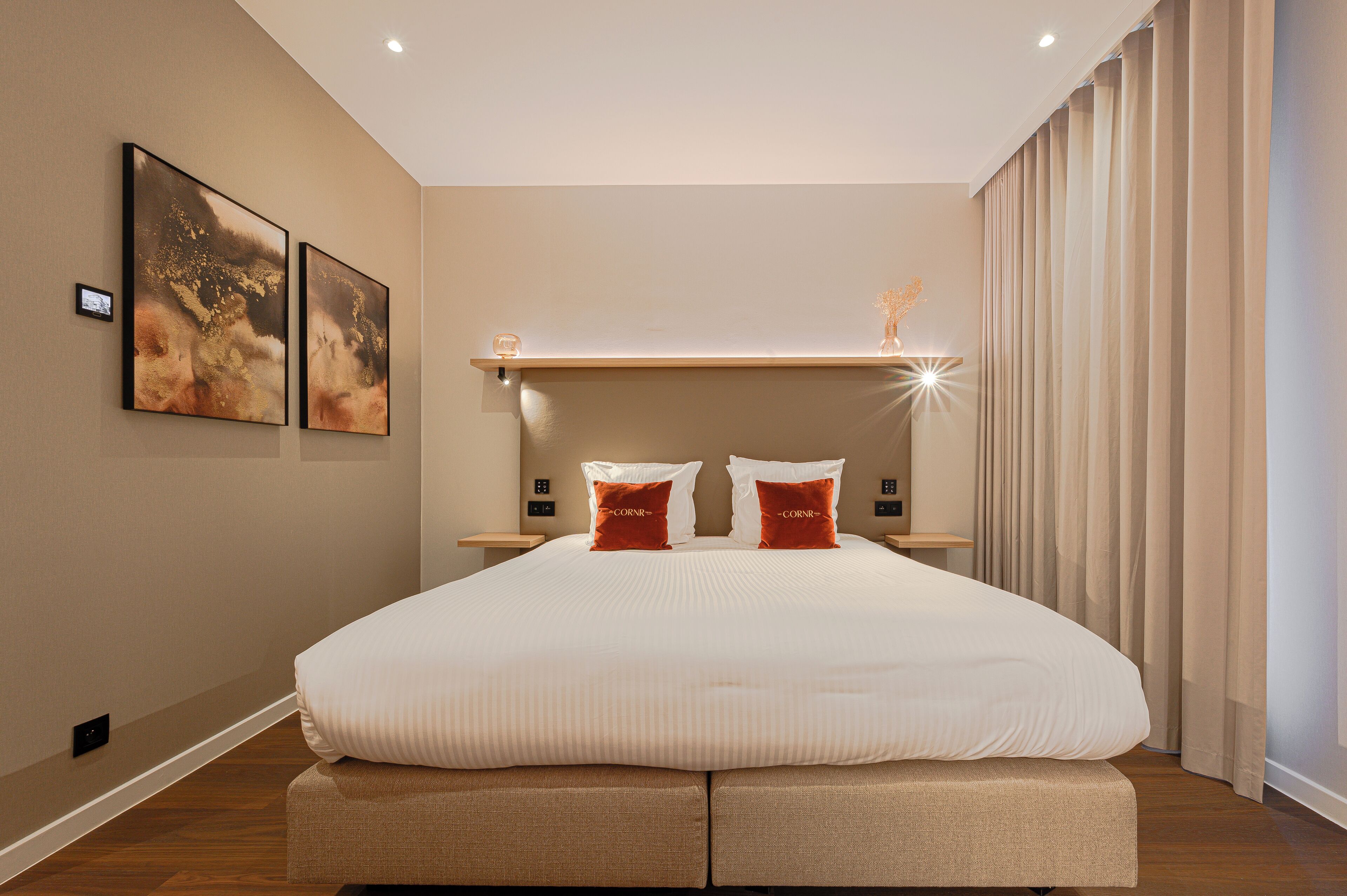 Una habitación de hotel moderna con una cama grande, dos mesitas de noche y un estante en la pared.