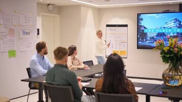 A conference room with a presentation screen displaying a building image and a whiteboard with text and charts.