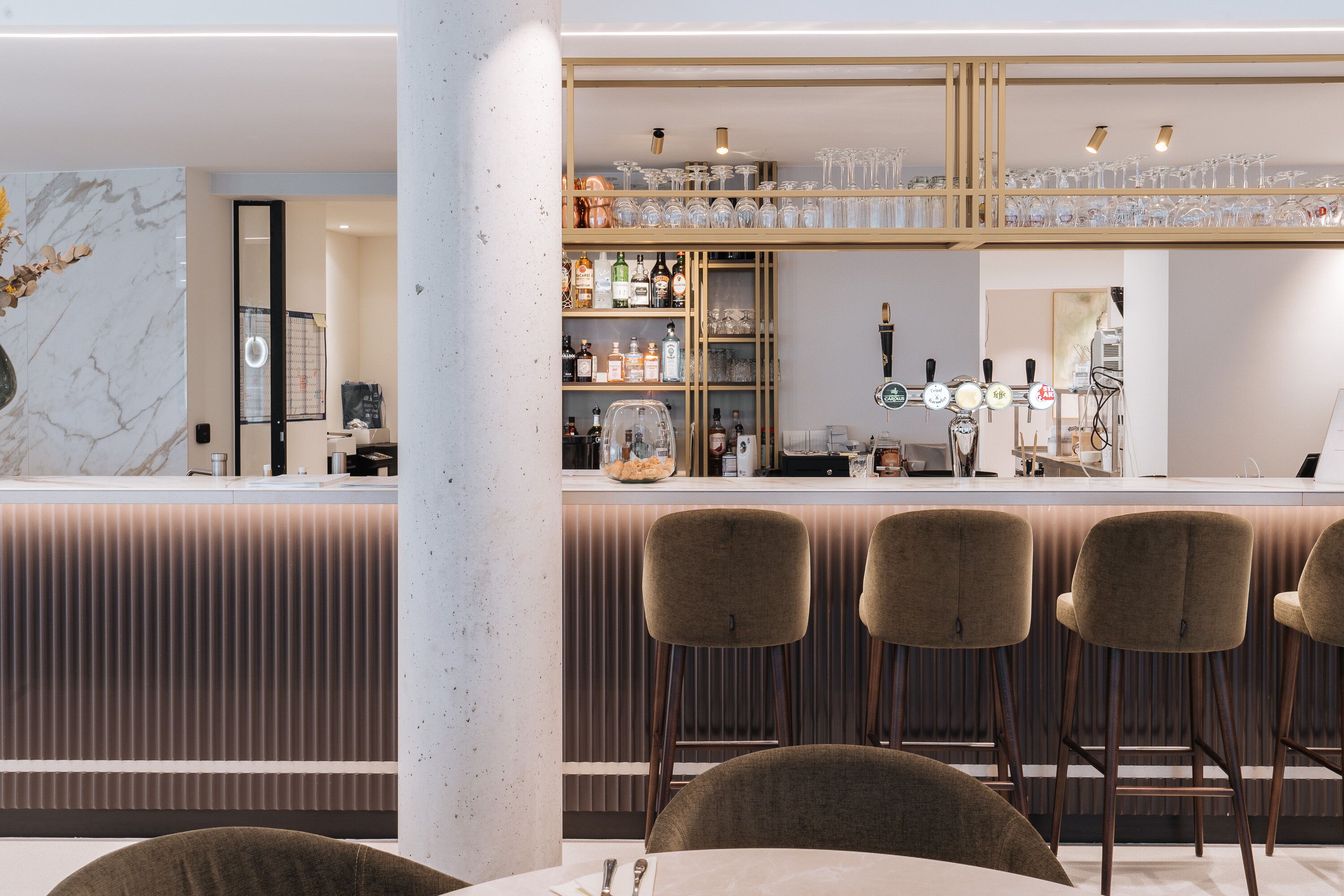 A modern bar area with a marble countertop, bar stools, and a variety of bottles and glasses.