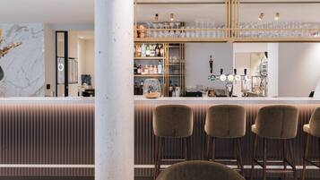 A modern bar area with a marble countertop, bar stools, and a variety of bottles and glasses.