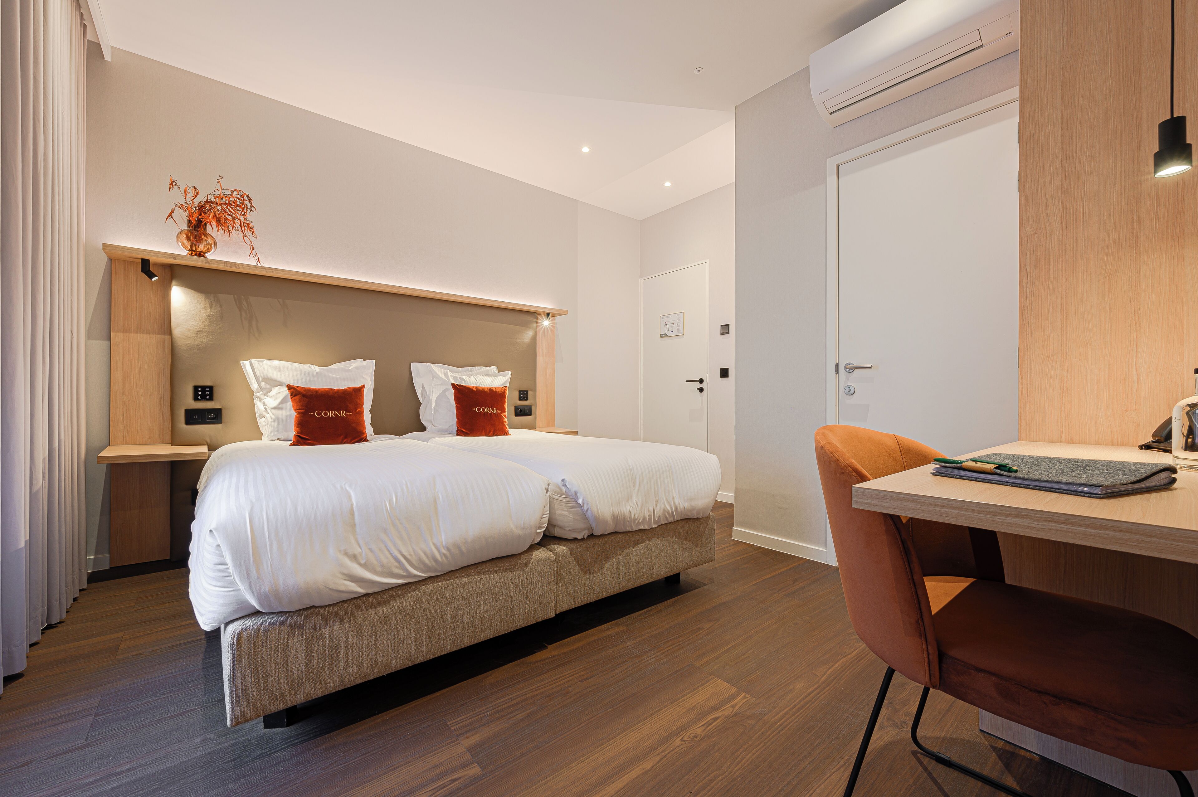 A modern hotel room with a bed, bedside table, and a desk with a chair.