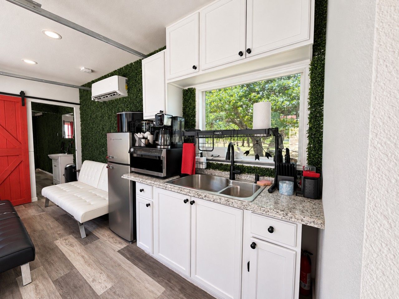 A compact kitchen with white cabinetry, a stainless steel sink, and a coffee machine.