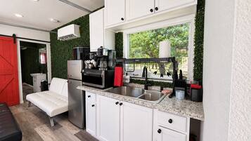A compact kitchen with white cabinetry, a stainless steel sink, and a coffee machine.
