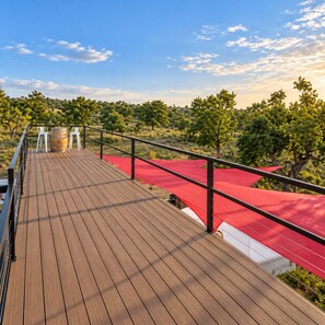 Eine Holzterrasse mit rotem Baldachin, weißen Stühlen und einem Fass.
