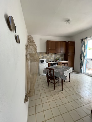 Uma cozinha compacta com armários de madeira, piso ladrilhado, mesa de jantar com cadeiras e uma janela com cortinas.