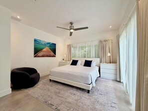 Une chambre à coucher moderne avec un lit, un ventilateur de plafond, une table de chevet, une lampe et un tableau au mur.