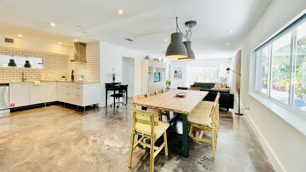 Une cuisine moderne avec une grande table à manger, des chaises en bois et un luminaire suspendu noir.