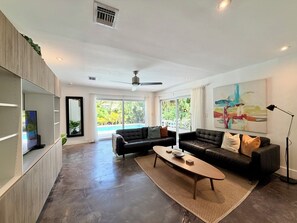 A modern living room with a sofa, coffee table, and a large window offering a view of a swimming pool.