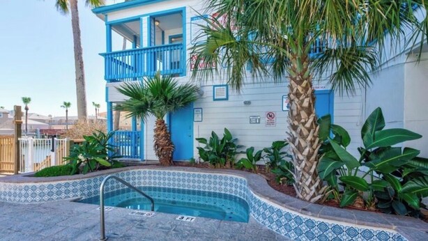 Un bâtiment à la façade bleue, une petite piscine bordée de carreaux et des plantes tropicales qui l’entourent.