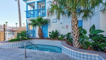A building with a blue exterior, a small pool with a tiled edge, and surrounding tropical plants.