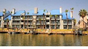 Un hôtel situé au bord de l’eau, doté de nombreux balcons, d’un quai et de palmiers.