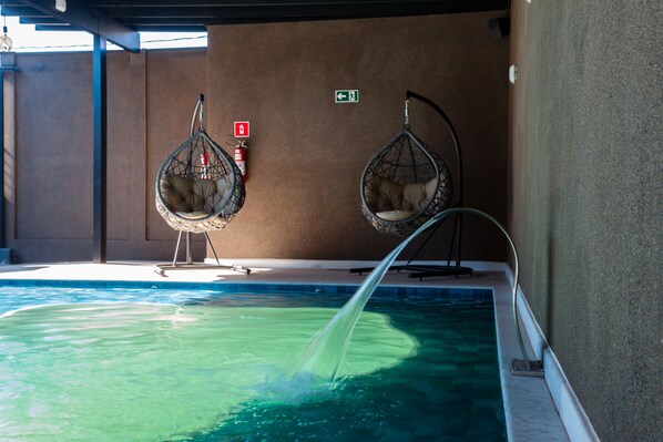 A swimming pool with two hanging chairs and a fire extinguisher on the wall. - SOPHITA BUSINESS HOTEL (Itaberá)