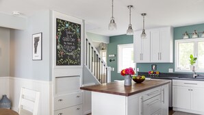 A kitchen with white cabinets, a wooden island, pendant lights, and a chalkboard with a positive message. - Tranquil lake house in VT w/ breathtaking views! (Grand Isle)