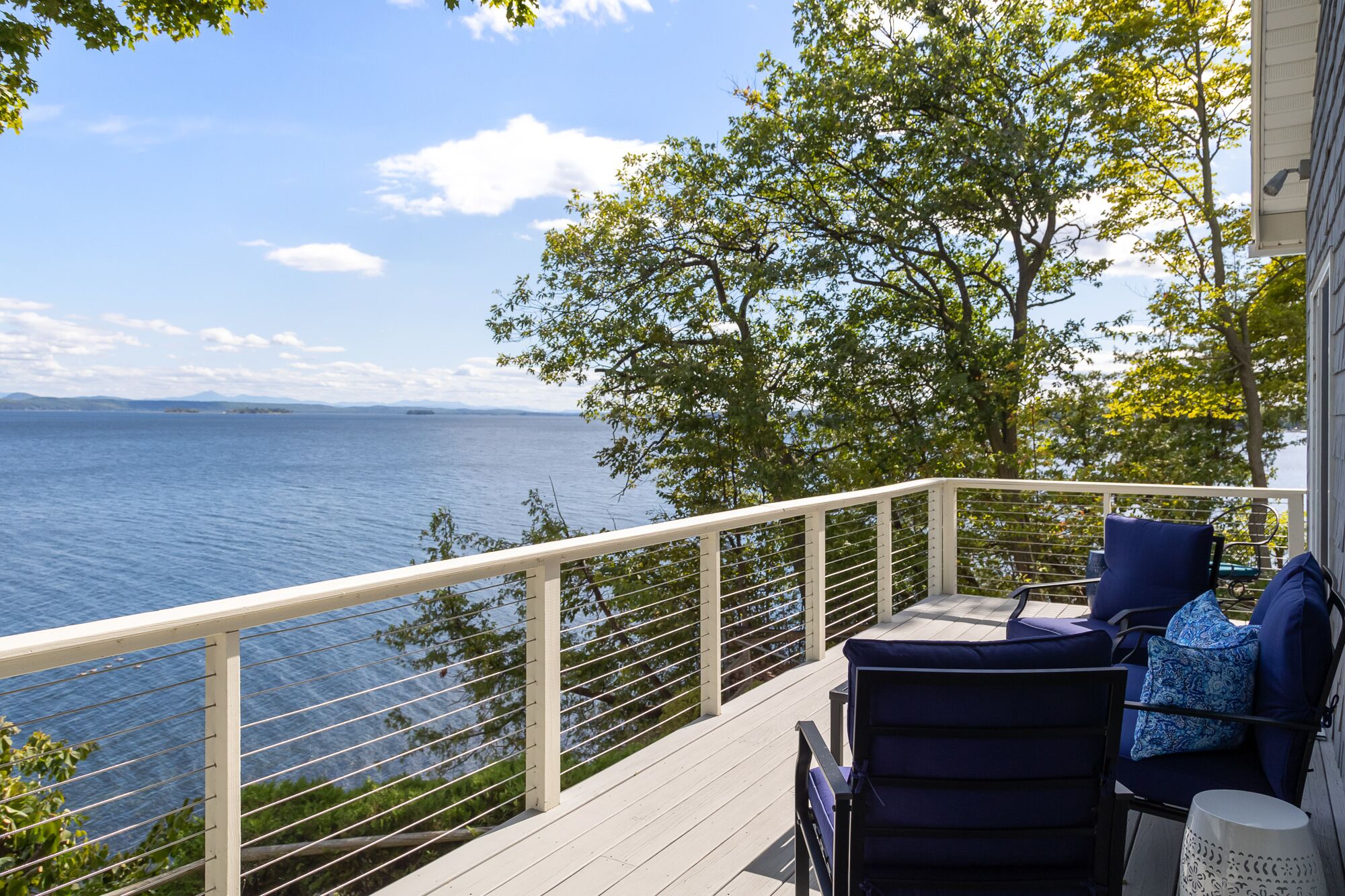 A deck with a railing overlooking a body of water, a chair, and a table with a lamp.