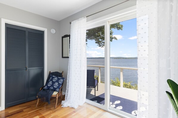 Een kamer met een grote glazen schuifdeur die uitkomt op een balkon met uitzicht op een meer en heuvels.