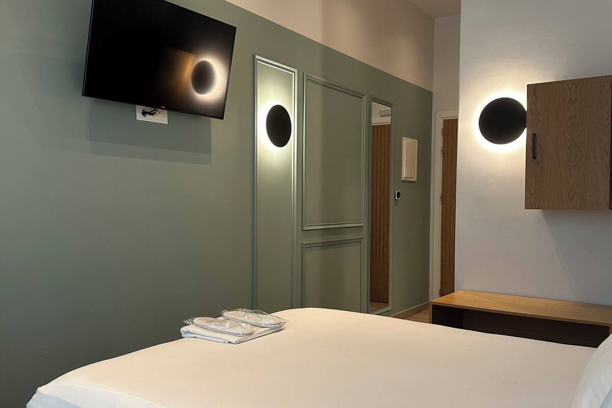 Una habitación de hotel moderna con una cama grande, un televisor de pantalla plana montado en la pared y una mesita de noche de madera.