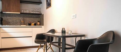 A modern kitchen with a dining area, featuring a marble floor, wooden ceiling beams, and contemporary furniture.