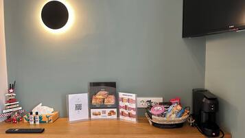 A reception desk with a flat-screen TV, a coffee machine, and a basket of snacks.