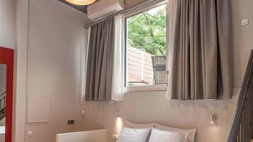 Un dormitorio con cama, suelo de madera, una ventana con cortinas, equipo de aire acondicionado y una escalera.