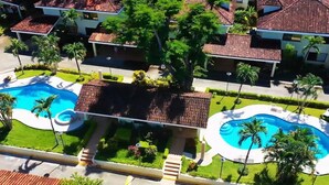 Ein Resort mit zwei Schwimmbecken, Palmen und einem zentralen Innenhof.