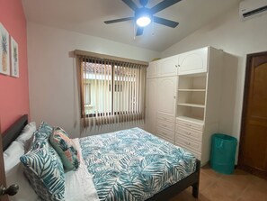 Ein Schlafzimmer mit Bett, Kleiderschrank, Deckenventilator und einem Fenster mit Jalousien.