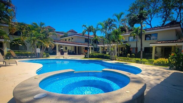 Ein Swimmingpool mit Whirlpool, umgeben von Palmen und einem Gebäude mit einem Ziegeldach.