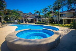 A swimming pool with a hot tub, surrounded by palm trees and a building with a tiled roof. - Beach Condo 3 Bed, Coco Beach, 2 Pools & GYM (Playa Del Coco)