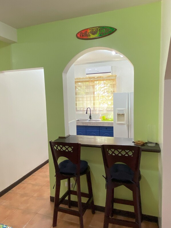 A small kitchen with a white countertop, two wooden chairs, and a window with a curtain.
