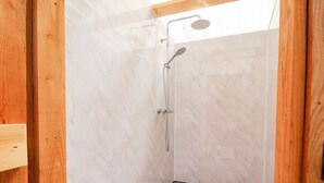 Ein kleiner, abgeschlossener Duschbereich mit Duschkopf und Handbrause, einem Holzrahmen und Fliesenboden.