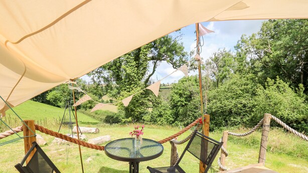 Ein Zelt mit Tisch und Stühlen, umgeben von einem Seilzaun und viel Grün.