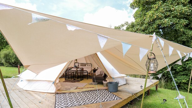 A tent with a wooden deck, a patterned rug, and a metal bucket. - Abercefel Retreat (Llandysul)
