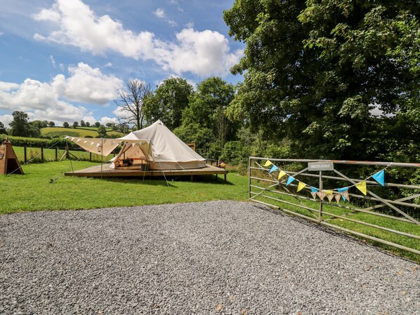 Ein Campingplatz mit Zelten und einer Holzterrasse, umgeben von Bäumen und einem Kiesweg.