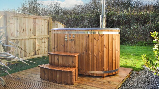 Een houten jacuzzi met treden en schoorsteen, omgeven door een houten terras en een gazon.
