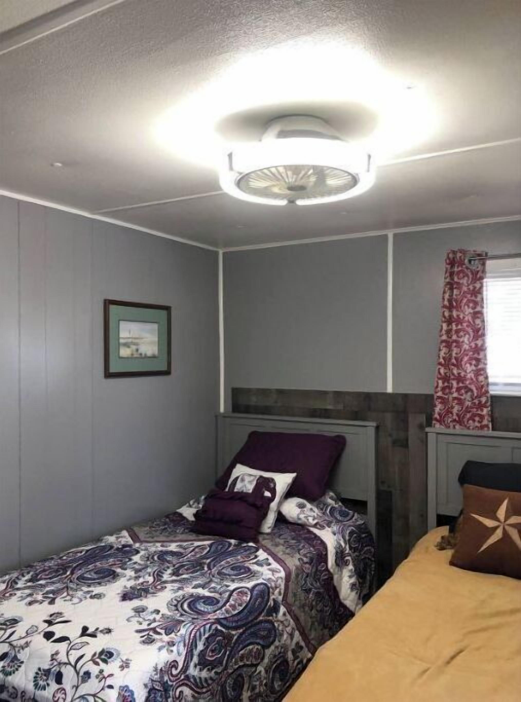 A bedroom with a bed, a headboard, a nightstand, a framed picture on the wall, and a window with curtains.
