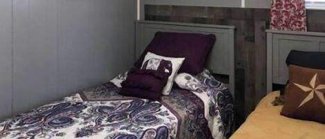 A bedroom with a bed, a headboard, a nightstand, a framed picture on the wall, and a window with curtains.
