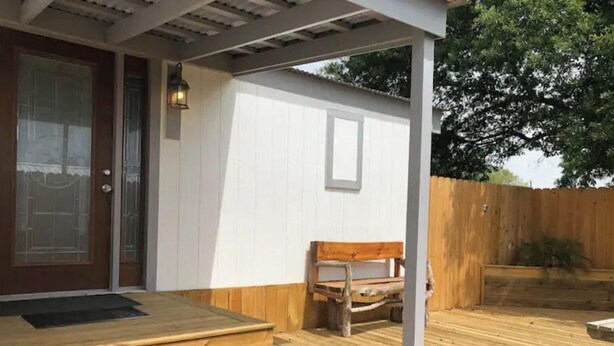 Eine Holzterrasse mit Stufen zu einer Tür, einer Bank und einem Holzzaun im Hintergrund.
